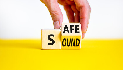 Safe and sound symbol. Businessman turns a wooden cube and changes the word 'safe' to 'sound' or vice versa. Beautiful yellow table, white background, copy space. Business, safe and sound concept. - obrazy, fototapety, plakaty