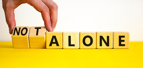 You are not alone symbol. Businessman turns wooden cubes and changes words alone to not alone....