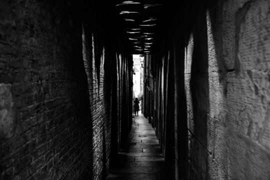 Grayscale shot of a person crossing a narrow dark tunnel