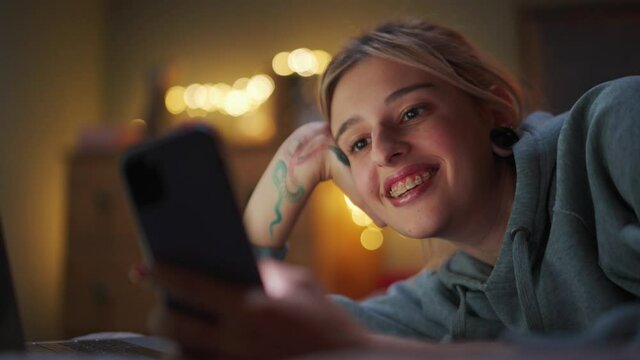 Smiling woman looking at phone on the bed at home