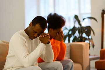 Upset pensive african american couple after fight sitting on couch separately thinking of family or...