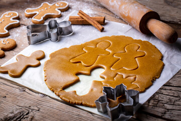 Hand cutting gingerbread dough with christmas metal cutters on wooden board, moody image. Making traditional christmas gingerbread cookies on rustic table with spices, decorations, rolling pin