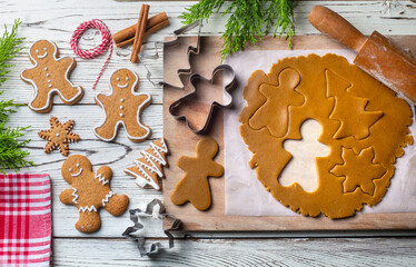 Hand cutting gingerbread dough with christmas metal cutters on wooden board, moody image. Making traditional christmas gingerbread cookies on rustic table with spices, decorations, rolling pin