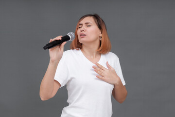Young beautiful woman singing a song into a microphone while standing on a gray background