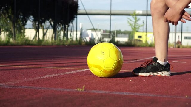 Close-up of a yellow soccer ball on an open sports ground next to a mans foot in a sneaker. Sports life concept, lifestyle activity