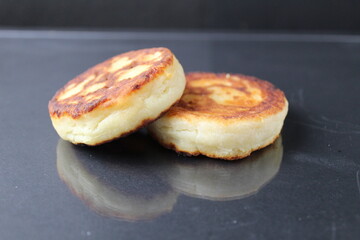 two cheesecakes of cottage cheese pancakes lie on top of each other side by side on a black background with a white sour cream sauce. Delicious healthy breakfast food. healthy eating. diet