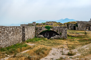 Ruins of ancient stone buildings in Shkoder Castle, Albania. Medieval stone walls among a yellow-green summer lawn in Rozafa fortress