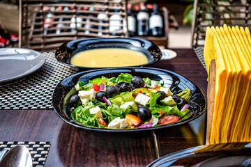 Black plate with Greek salad in a restaurant in Tirana, Albania, close-up. European seasonal dish with lettuce, tomato, cucumber, green pepper, olives and feta cheese