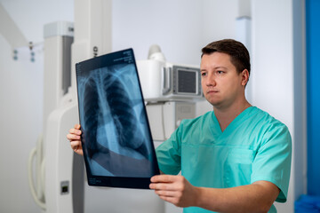 Naklejka na ściany i meble Young serious competent male doctor looking at X-ray at doctor's office. Computer tomography background. Stock photo