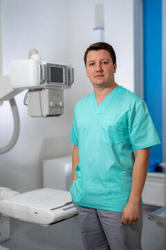 Young serious competent male doctor looking at the camera at doctor's office. Computer tomography background. Stock photo