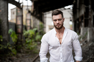 Fashion and stylish young male posing on broken building background. Handsome man in white shirt looking at the camera