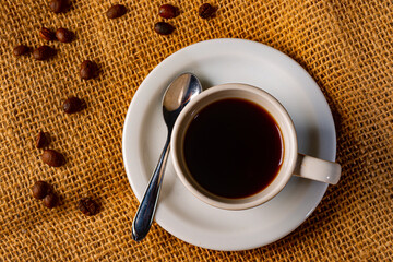 Cup of coffee served on a jute tablecloth with raw Brazilian coffee beans around