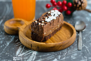 Delicious chocolate cake with winter decor snowflakes on a wooden plate with a spoon, a glass of juice and Christmas decor on a gray background.