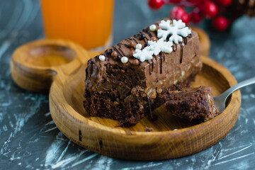 Appetizing slice of chocolate brownie in a spoon, brownie on a wooden plate, glass of multifruit juice and new year's decor on the background