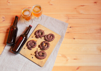 Roasted sausages on cutting board, beer bottles and beer glasses near on wooden table.