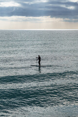 Unrecognizable person practicing paddle surfing Young athletic silhouette paddling stand up paddleboard. Healthy lifestyle.