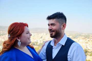 Caucasian plus size red headed woman and her turkish beloved man look to each other. Mixed race couple on a romantic date. Woman looks at her bridegroom smiling. Marriage or engagement