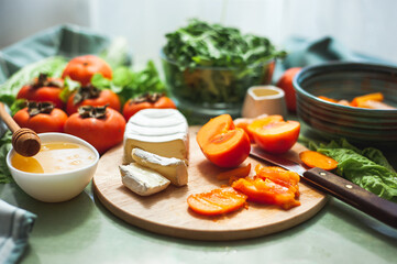 Ingredients and the process of making a vitamin winter salad with persimmons, tangerines and cheese. Selective focus Vegan salad preparation. Healthy eating.