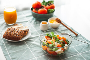 Vegan breakfast or lunch. Light sweet and sour salad with persimmon, tangerines and cheese. Winter vitamin salad on white table with a green napkin Diet food. Selective focus 