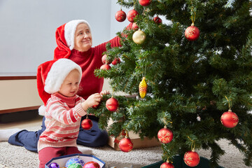 Merry Christmas and Happy Holidays. Happy family grandma and granddaughter cheerfully decorate the Christmas tree at home. A grandmother and a small child are having fun near a tree indoors