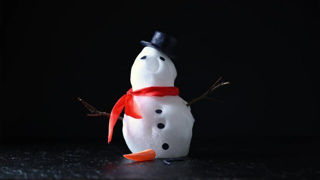 Funny snowman in stylish hat and red scalf melting on black background. Studio timelapse video. UHD 4K time lapse