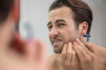 Young man shaving and looking disturbed