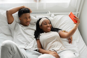 attractive african male with female lie in bed with mobile phone 