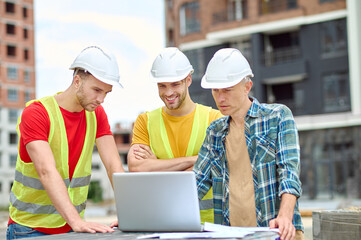 Fototapeta premium Three men looking into laptop at construction site