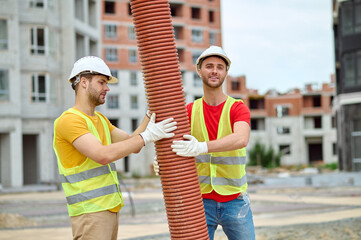 Two workers holding pipe at construction site