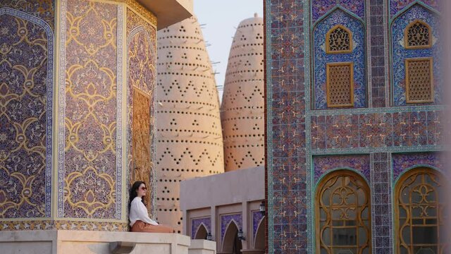 tourist woman sitted at Blue mosque of Katara village made of colorful mosaic in Doha Qatar showing Pigeon tower behind
