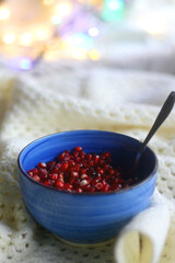 Blue ceramic bowl with fresh pomegranate seeds, soft knitted blanket and colorful bokeh lights. Hygge at home. Selective focus.
