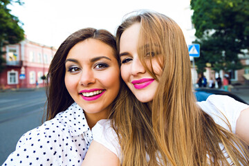 Summer sunny image of two sisters best friends brunette and blonde girls having fun on the street