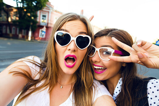 Summer sunny image of two sisters best friends brunette and blonde girls having fun on the street