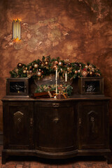 an old chest of drawers on which there are burning candles against the background of kinship ornaments on spruce branches, decorated with balls and a gift next to them. beautiful christmas background