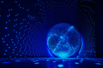 Large disco ball reflecting blue light. Dark hall for discos. Copy space.