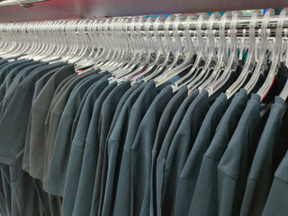 a row of plastic transparent hangers with dark monochrome t-shirts on a shiny metal rack 