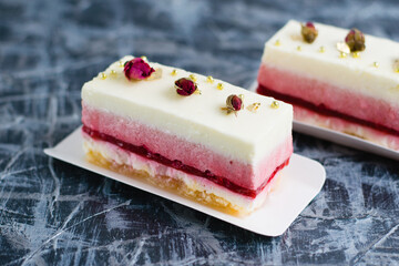 Two delicious mousse cakes with decorative roses on a gray background side view.