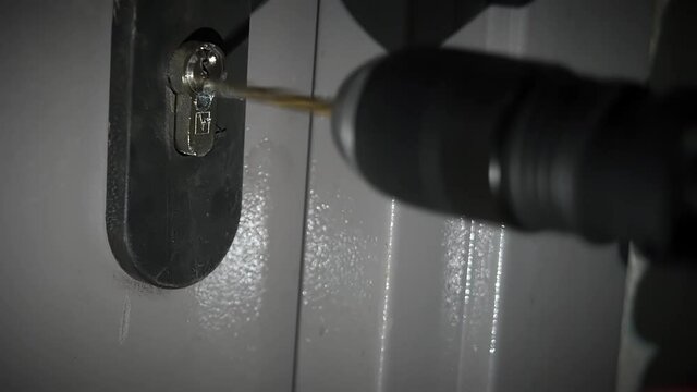 Breaking a door lock with a drill. A man drills a keyhole to open the door. Thief trying to break the door lock in the dark