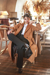 Pensive young asian lady in beige coat and business suit sitting in cafe at meeting