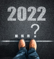 2022 new year. Feet of a man in yellow boots against the background of the inscription on the asphalt 2022 and a question mark.