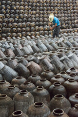 Man in the middle of big pile of wine jars stacked up at a local rice winery, Wuxi, Jiangsu...