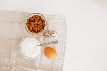 Nuts almonds, sour cream or yogurt, chicken and quail eggs on a linen kitchen towel on a white table. Healthy food and nutrients for proper nutrition of the brain and body concept