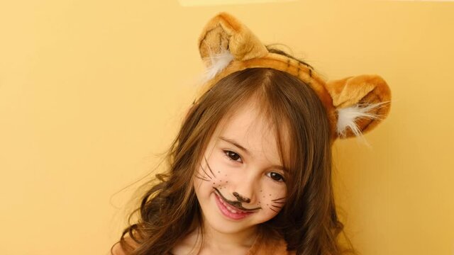 A girl with long hair, a hat with ears in the image of a tiger turns around. Cute beautiful baby with painted face