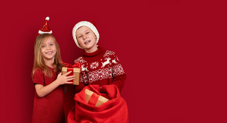 Fototapeta premium Children are standing on red background boy gives girl big gift from Santa's bag