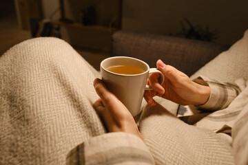 A cup of tea in the hands of a girl. The girl is drinking hot tea. A girl in pajamas is wrapped in...
