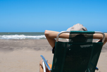 person with hat relaxing on the beach looking at the sea with copy space