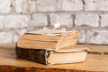 Two old books in a battered binding are lying against a brick wall made of light brick. Close-up,...