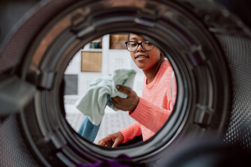 Woman does laundry, reaches inside washing machine, takes out colored clothes after spinning, puts...