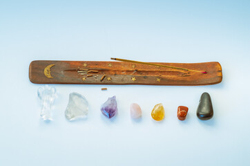 Flat lay of incense stick burning and 7 healing crystals aligned by chakra on blue background	