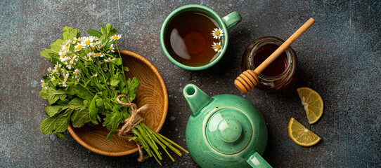 Herbal tea with camomile, fresh medical herbs and flowers, tea cup, tea pot, jar of honey, lemon...